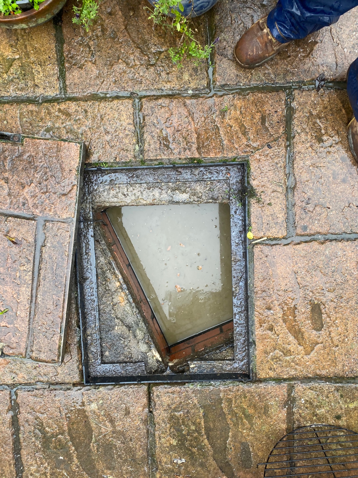 Outside drain chamber in a Hythe, Kent, garden paved area backed up and filled with stagnant water before drain unblocking by First Response Drains